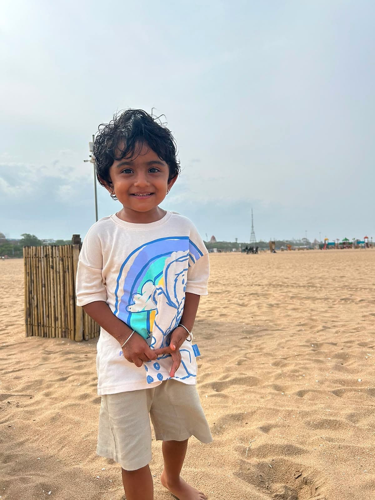 A young child standing barefoot on the sand, smiling at the camera.