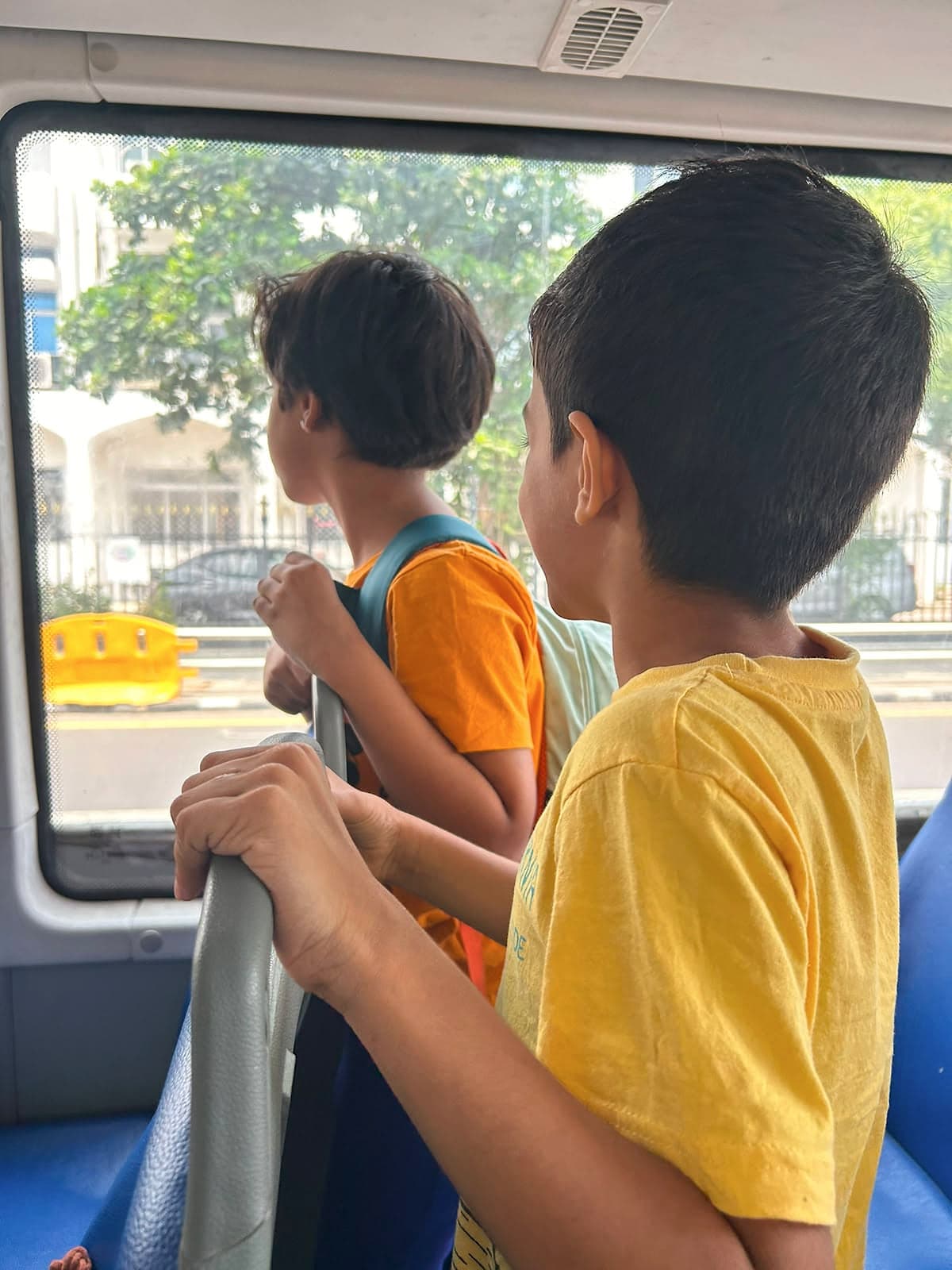 Two children standing in a bus, holding the seat rail and looking out of the window.